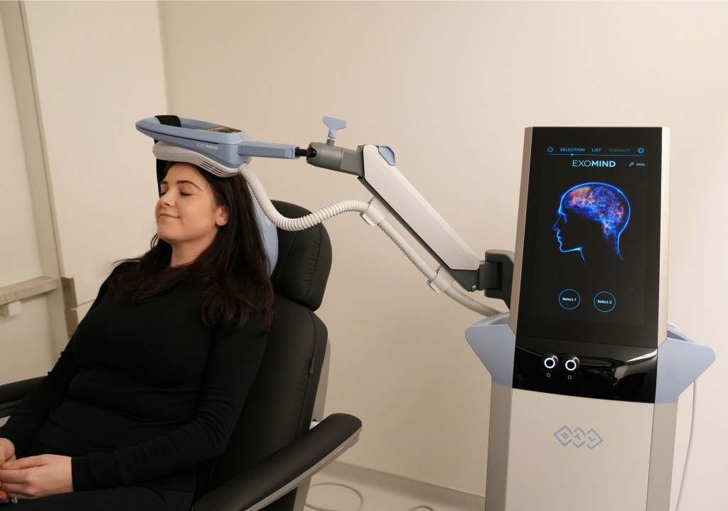 A patient sitting in a chair with a non-invasive, exomind brain stimulation device.